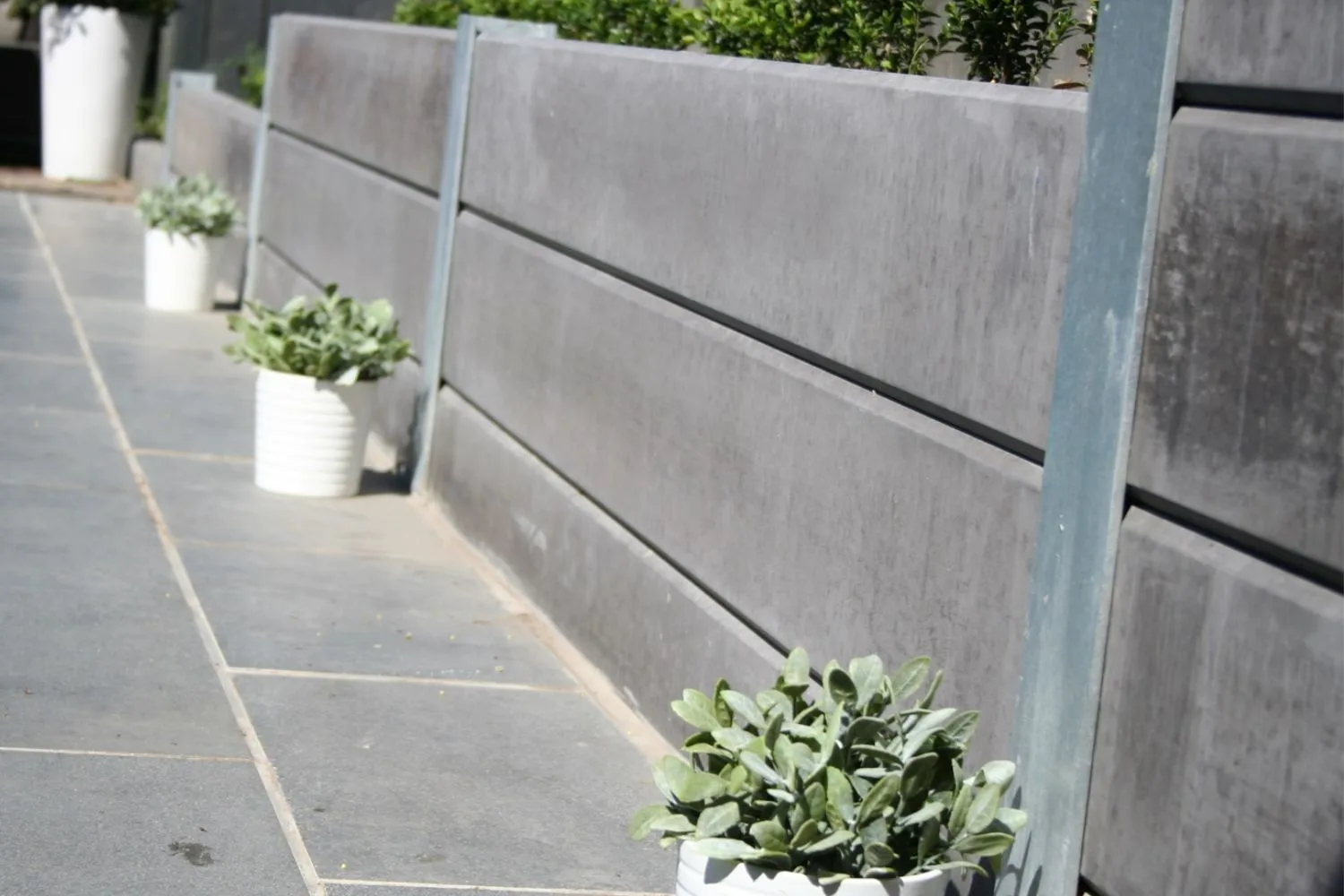 Grey concrete sleeper retaining wall beside a paved courtyard with potted plants