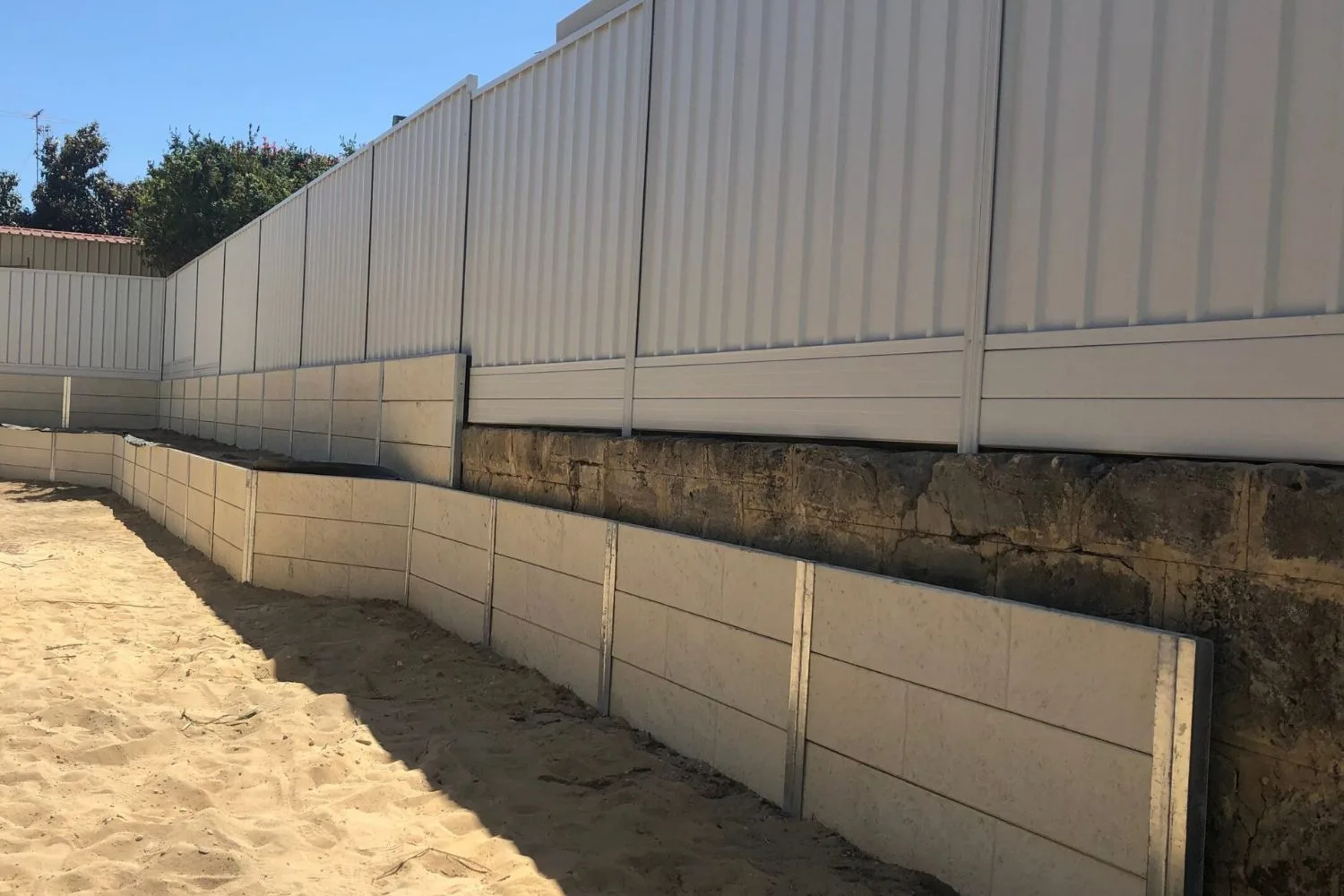 Two-tier concrete sleeper retaining wall built along a boundary fence
