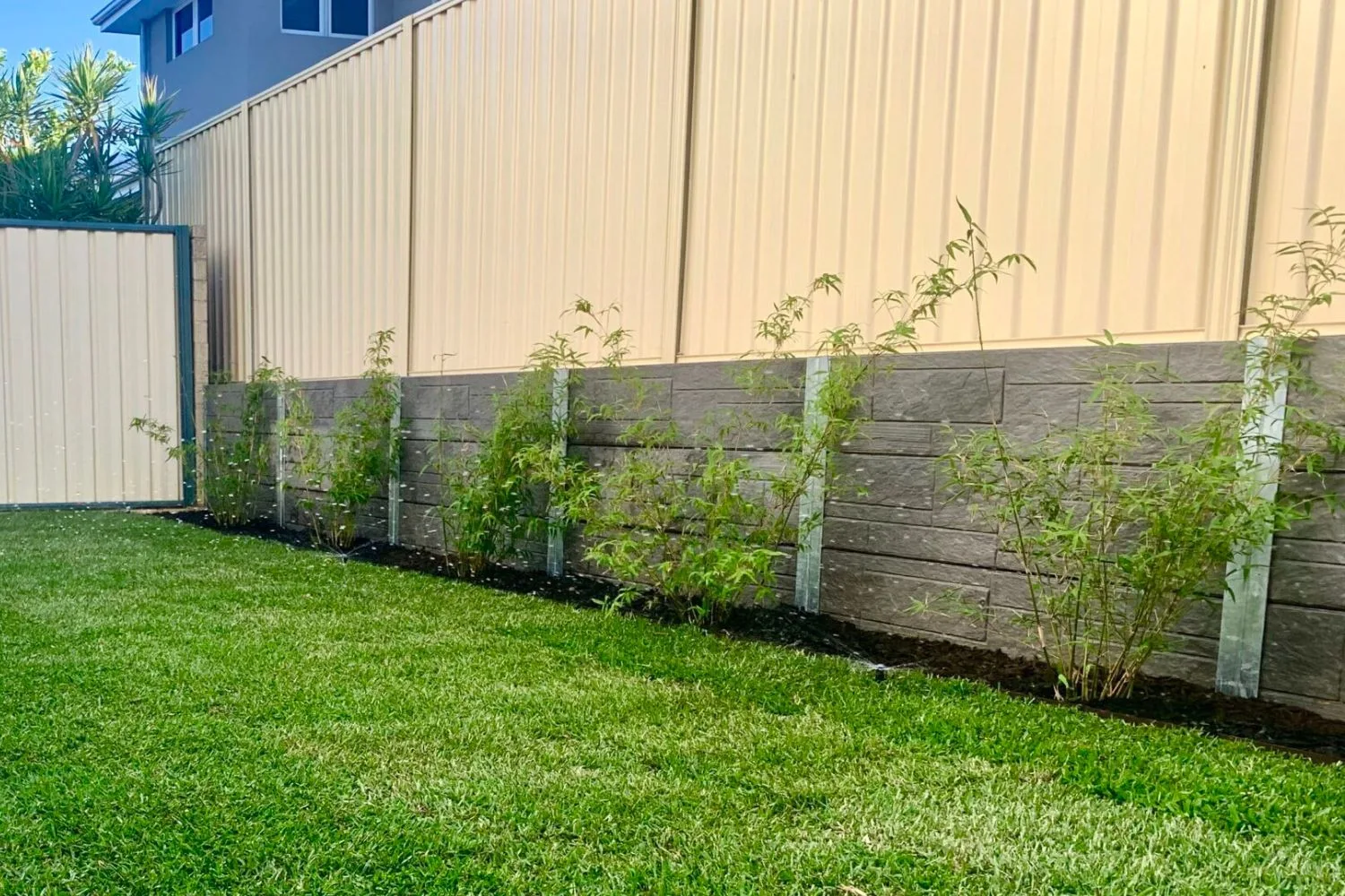 Concrete sleeper retaining wall with garden planting along a black boundary fence