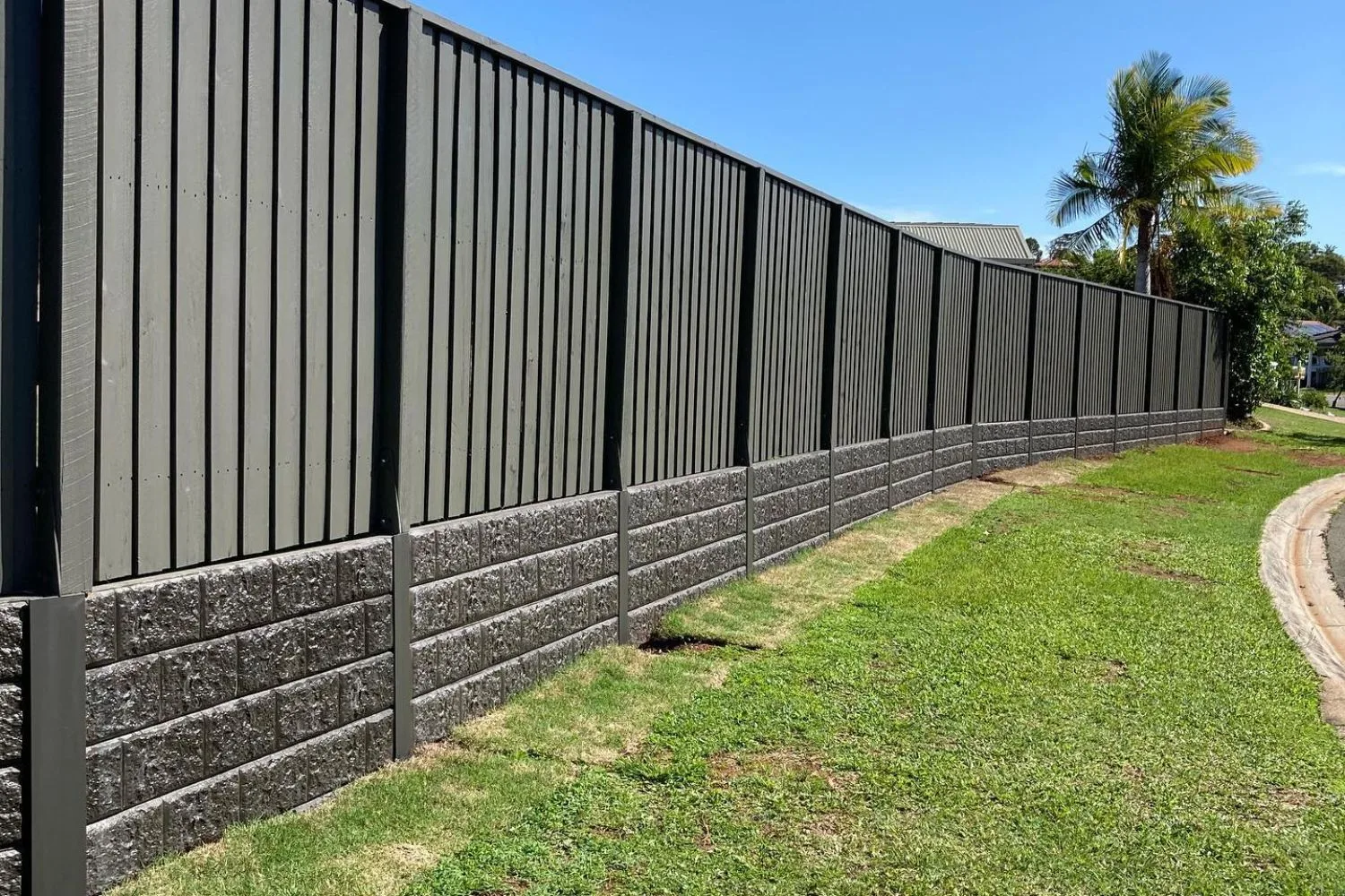 Concrete sleeper retaining wall with black steel posts along a lawn and fence line