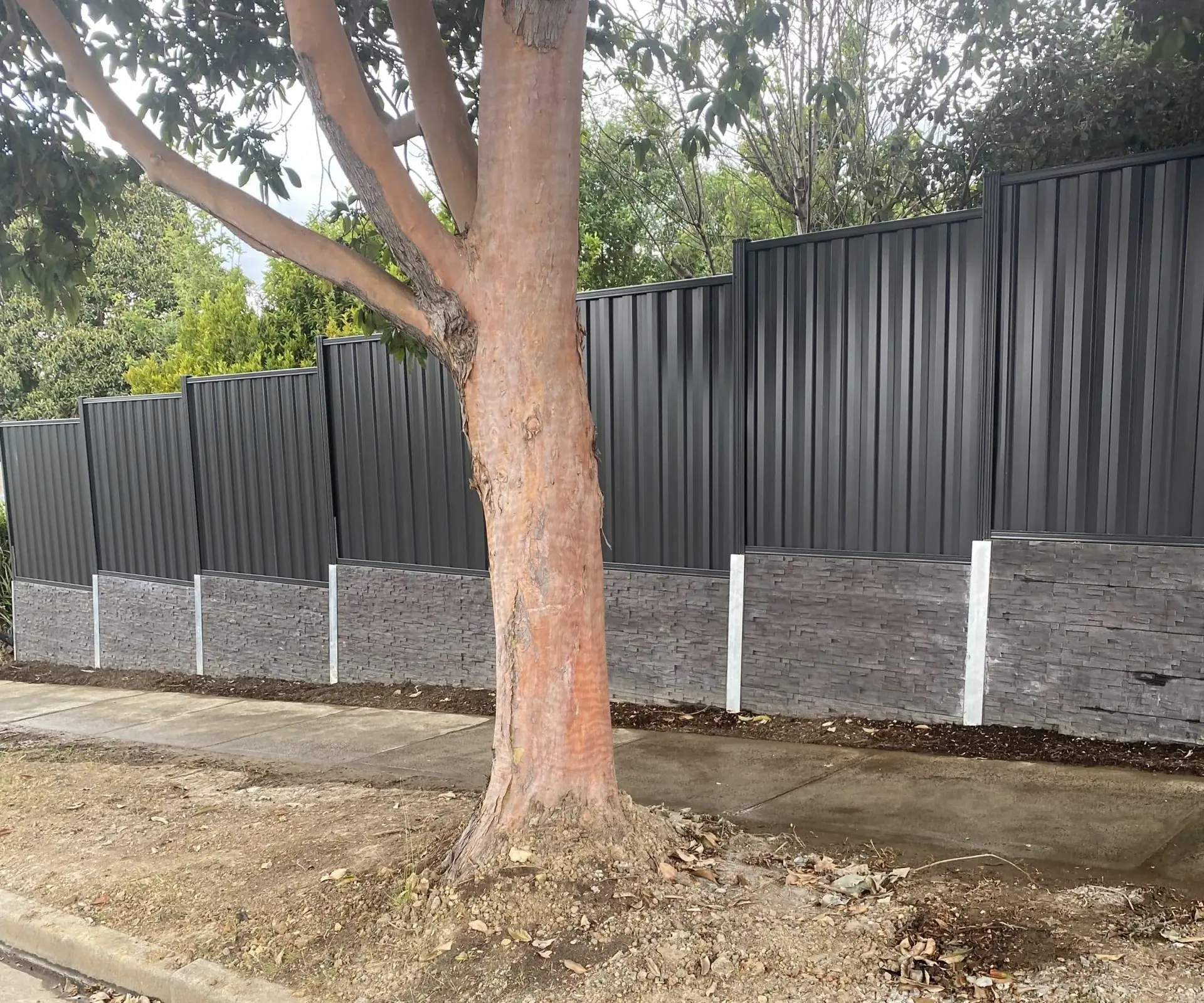 Charcoal concrete sleeper retaining wall beside a large gum tree