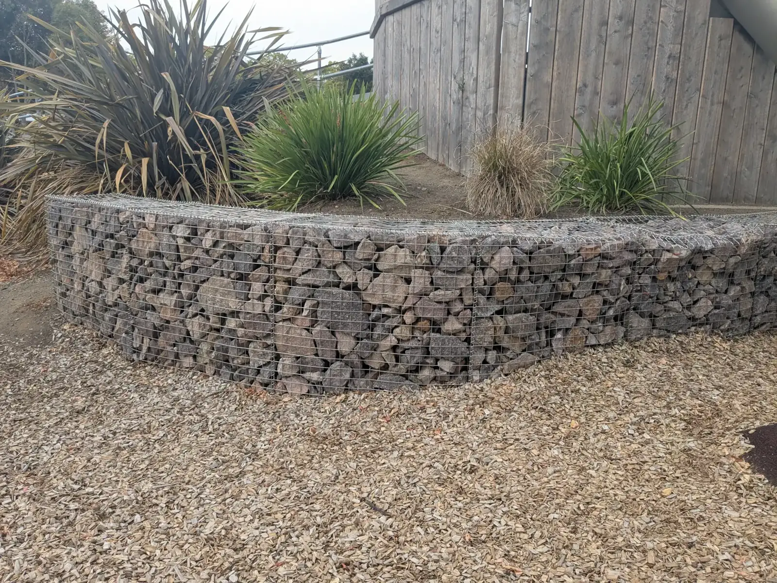Curved gabion retaining wall filled with stone beside a gravel path