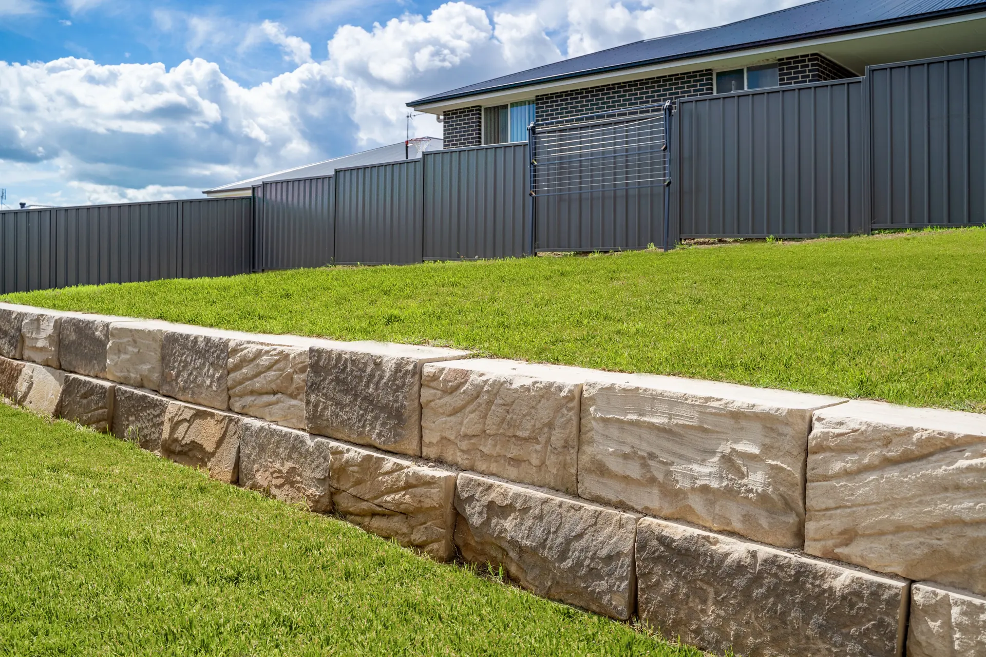 Large sandstone block retaining wall along a lawn in front of a home