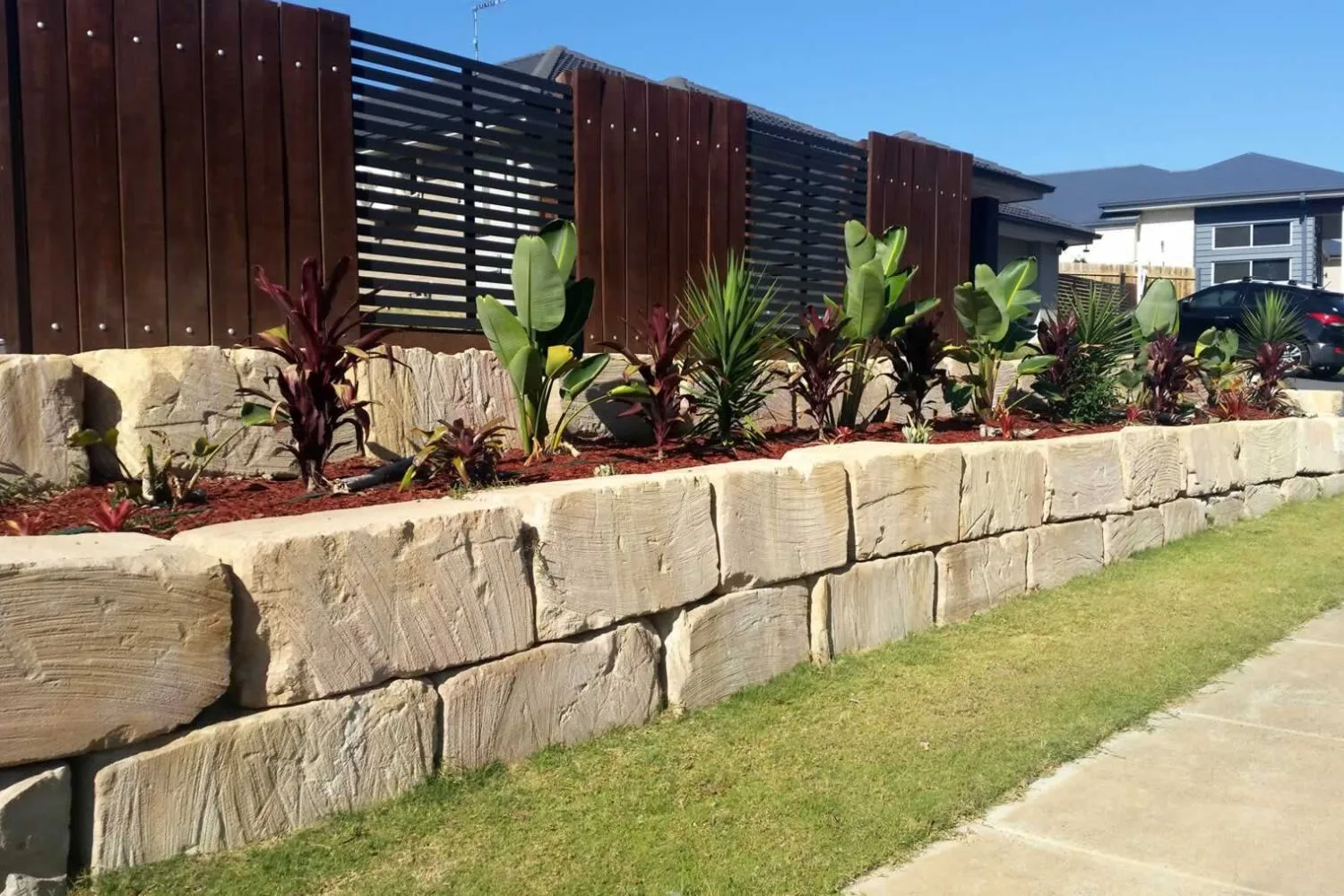 Sandstone block retaining wall with tropical planting along a front yard